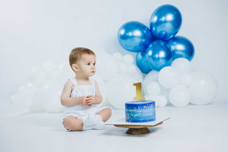 Baby boy with blue cake and balloons during smash the cake photoshoot.