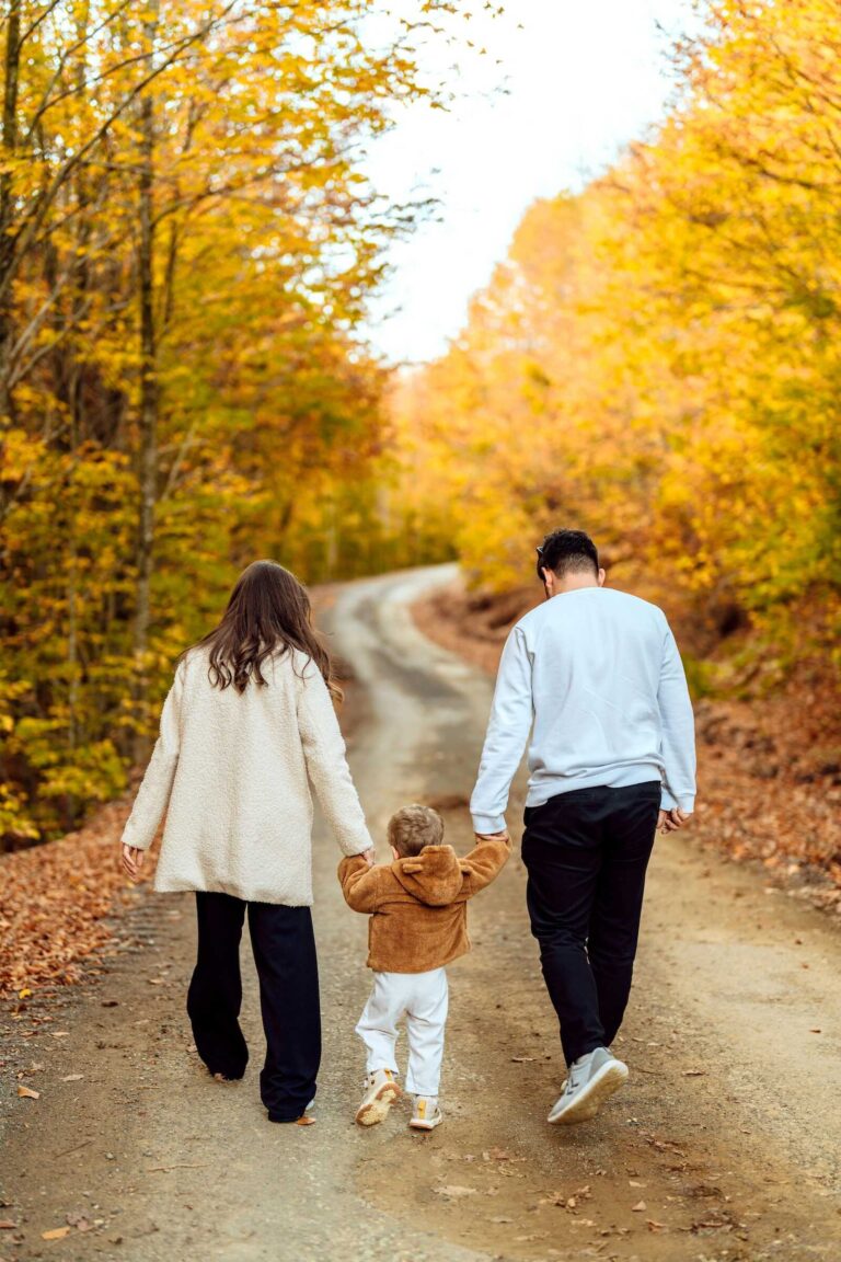 Family walking down autumn road holding hands during fall family photos.