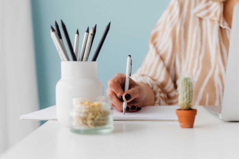 Woman writing in a notebook at a clean desk with pencils and decor, representing intentional planning.