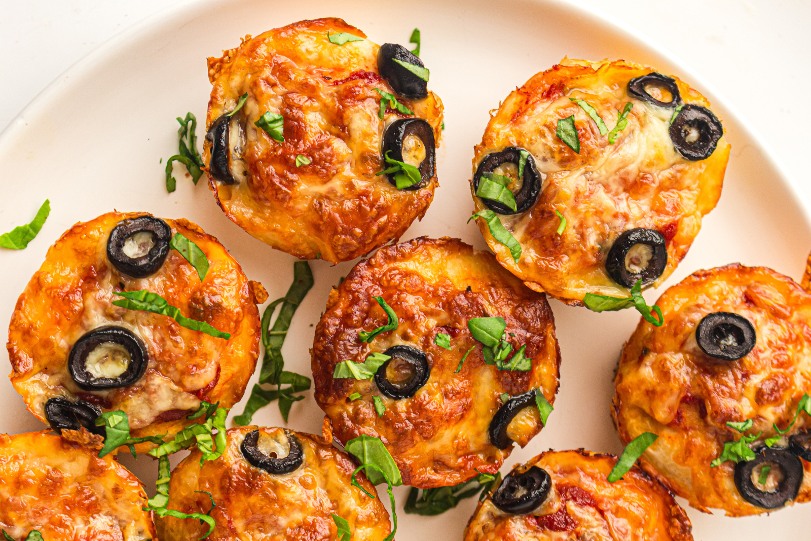 Homemade lunchbox mini pizzas with cheese, black olives, and fresh basil.