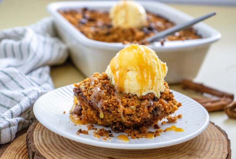 A slice of homemade pumpkin crisp topped with vanilla ice cream and caramel sauce on a white dessert plate.