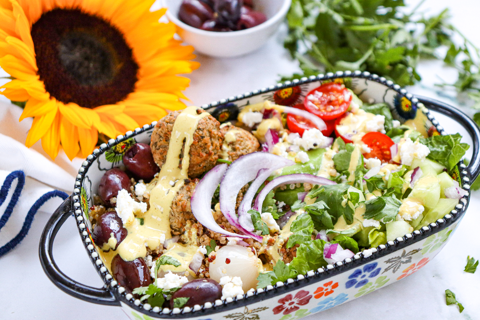 Mediterranean falafel bowl with quinoa, fresh vegetables, feta, olives, avocado, and creamy dressing.